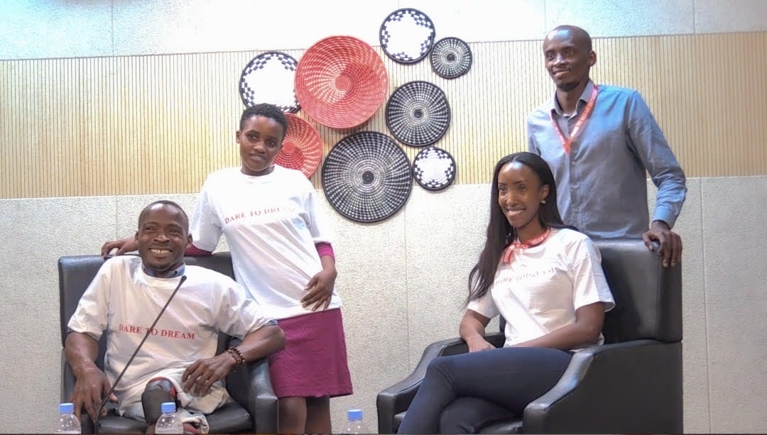 Smiling advocate with microphone in Dare to Dream shirt with traditional Rwandan Imigongo backdrop
